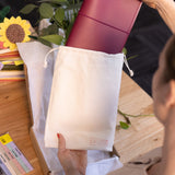 Person holding a red notebook over a white bag with a plant and books in the background