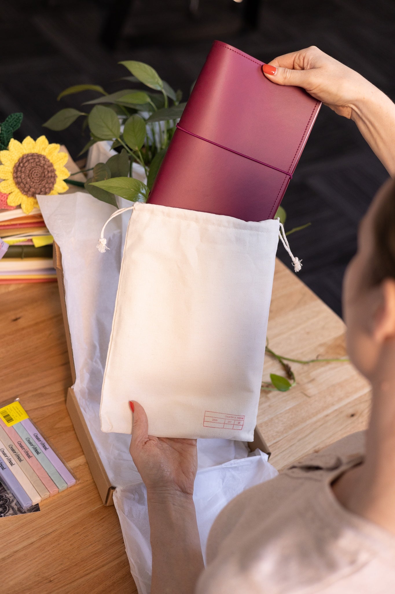 Person holding a red notebook over a white bag with a plant and books in the background