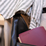 Black leather bag with a maroon NOTEBOOK FOLIO, against a blurred background.