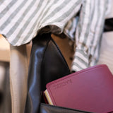 Black leather bag with a maroon NOTEBOOK FOLIO, against a blurred background.
