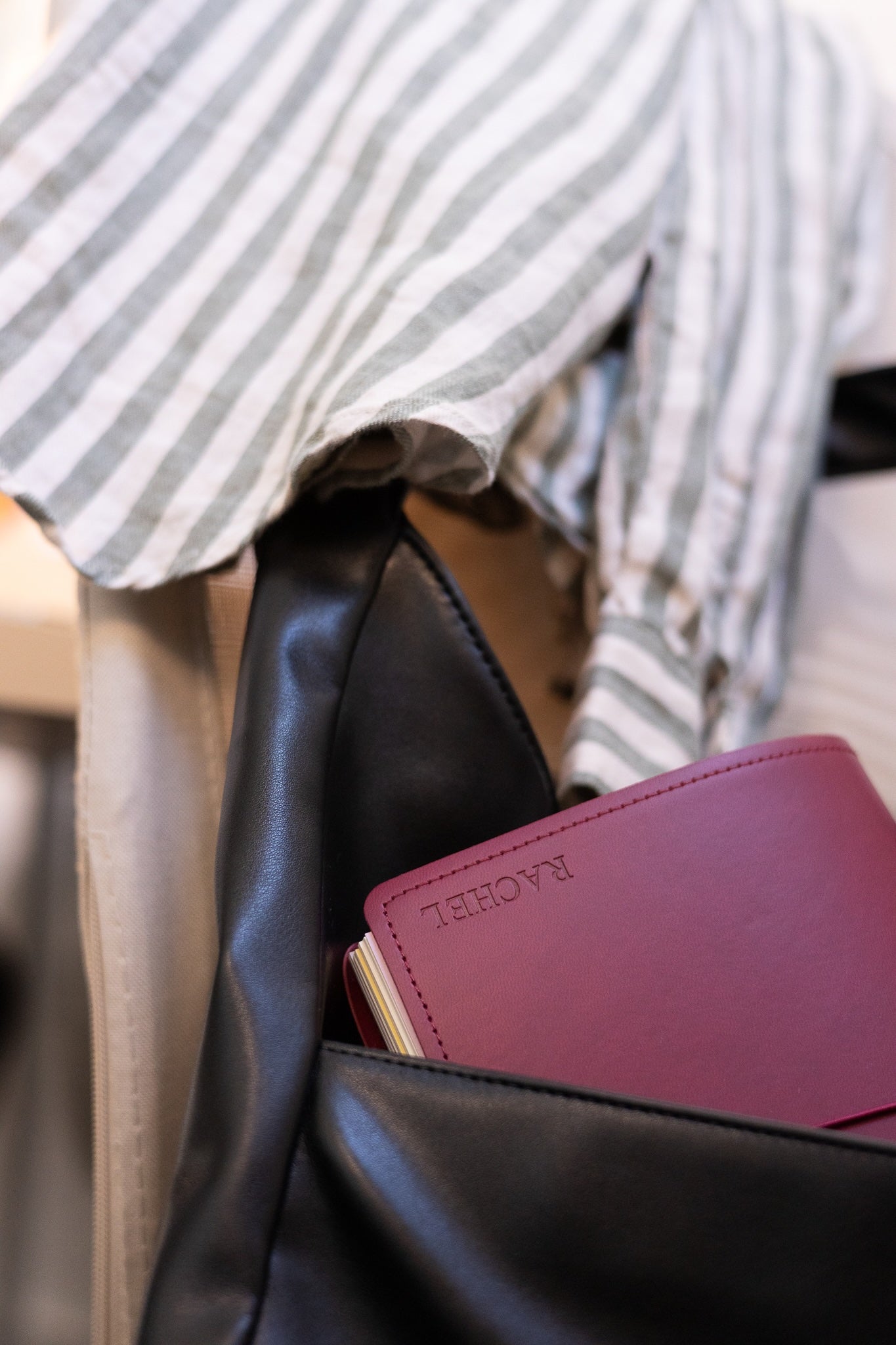 Black leather bag with a maroon NOTEBOOK FOLIO, against a blurred background.