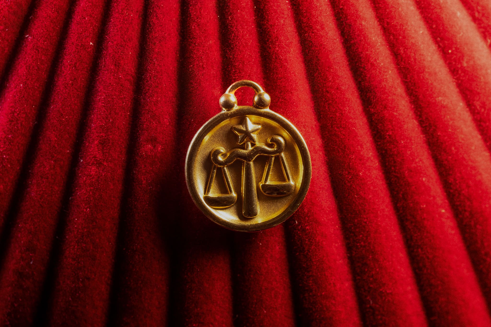 Gold Libra zodiac pendant on a red textured background