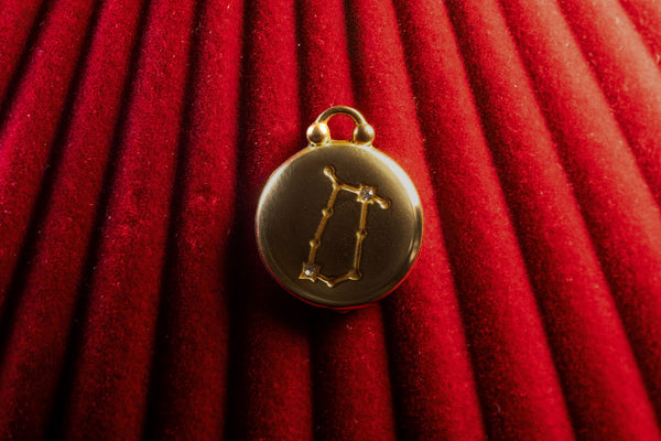 Gold pendant with a Gemini Constellation on a red textured background